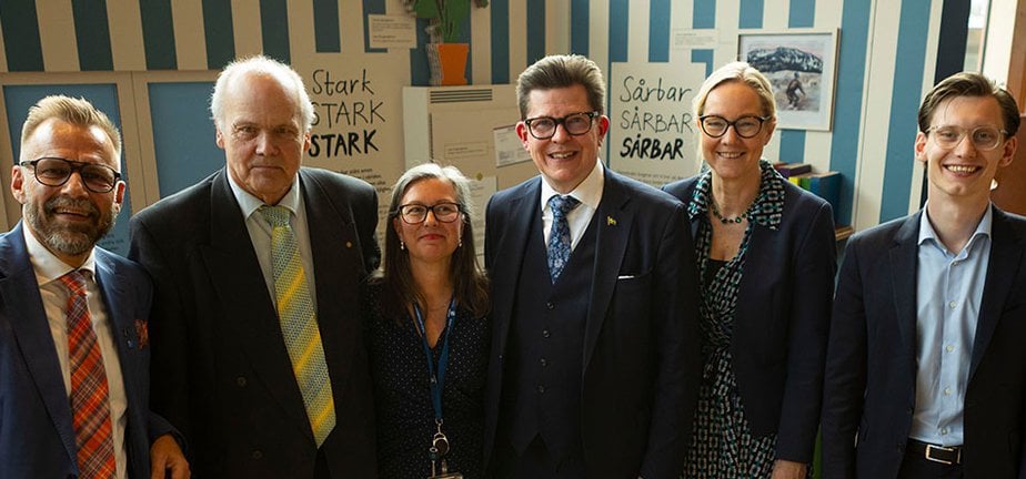 Leende personer som står i bredd framför en utställning om demokrati
