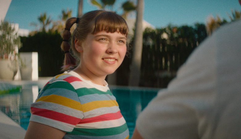 Flicka i randig tr&ouml;ja st&aring;r vid en pool och pratar med n&aring;gon.