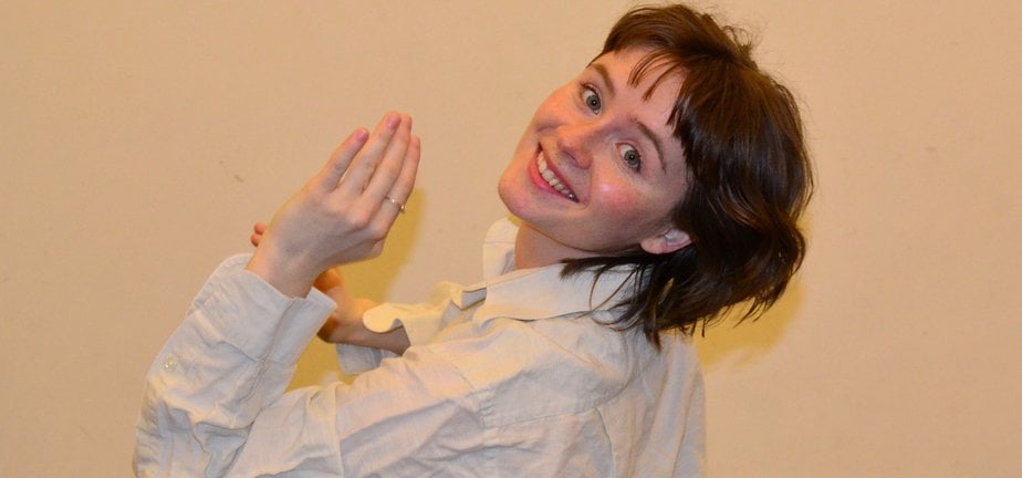 Kvinna med brunt hår och i vit skjorta som vrider sig mot kameran