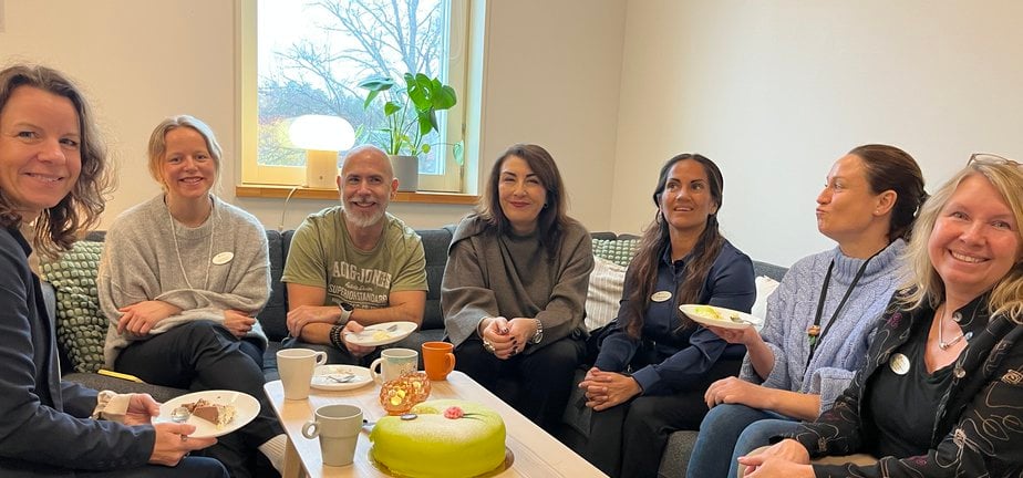 En grupp människor som sitter runt ett bord och fikar med tårta.