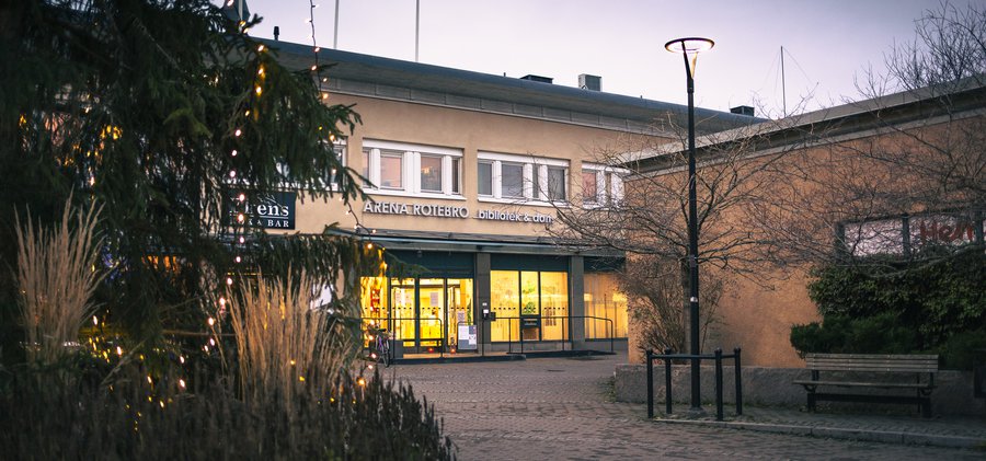 En byggnad som har träd och buskar med ljusslingor i sig utanför entrén. 