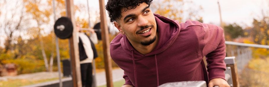 En man i rödbrun huvtröja lutar sig mot ett trästaket.