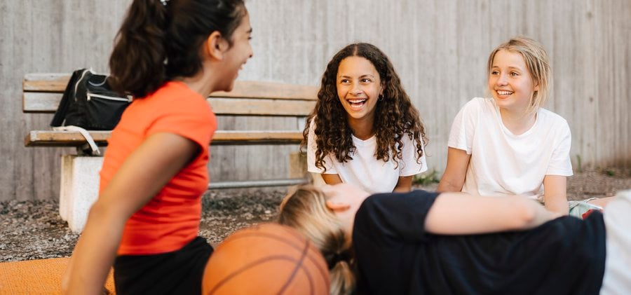 Tre flickor som sitter och skrattar med basketboll