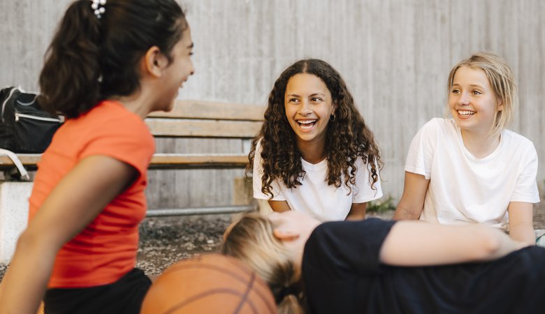 Tre flickor som sitter och skrattar med basketboll