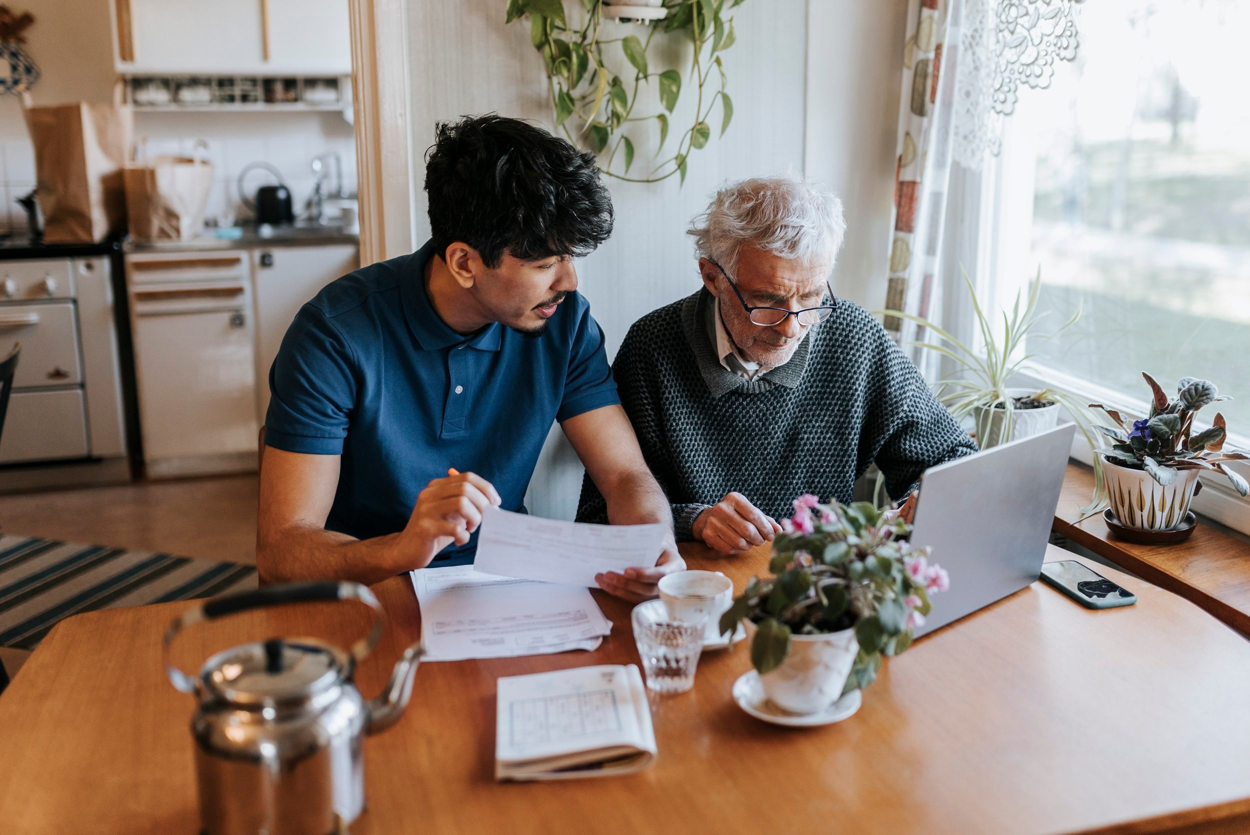 Male caregiver discussing medical reports with senior man using laptop at home