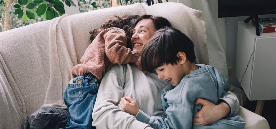 Playful boy and girl with mother on sofa at home