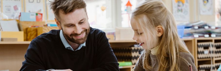 Leende manlig lärare hjälper elev i klassrum