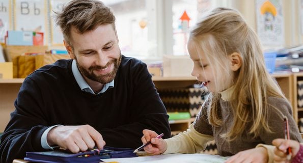 Leende manlig lärare hjälper elev i klassrum