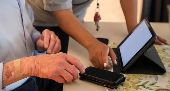 Äldre man får hjälp med digital teknik av kvinnlig vårdpersonal