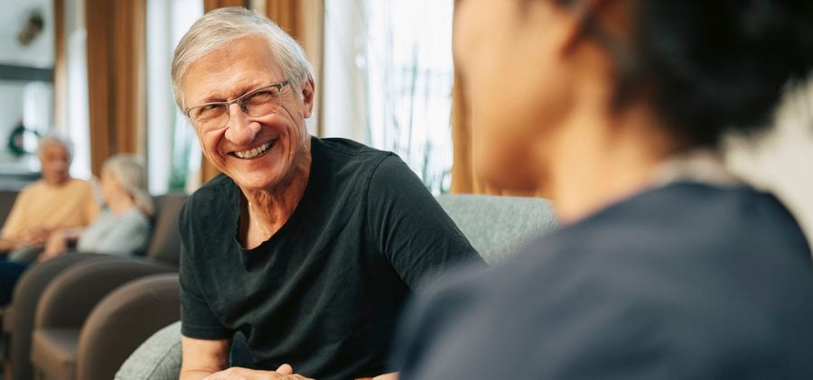 Happy senior man talking with female nurse while sitting at nursing home