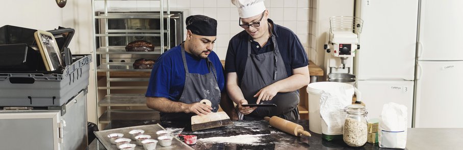 Young man showing digital tablet to coworker while cooking in kitchen