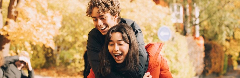 Cheerful teenage girl piggybacking male friend outdoors