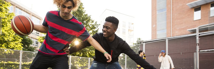 Young man taking basketball from male friend while playing in sports field