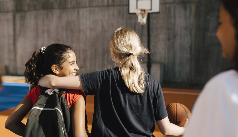 Blond girl with arm around female friend while walking in basketball court
