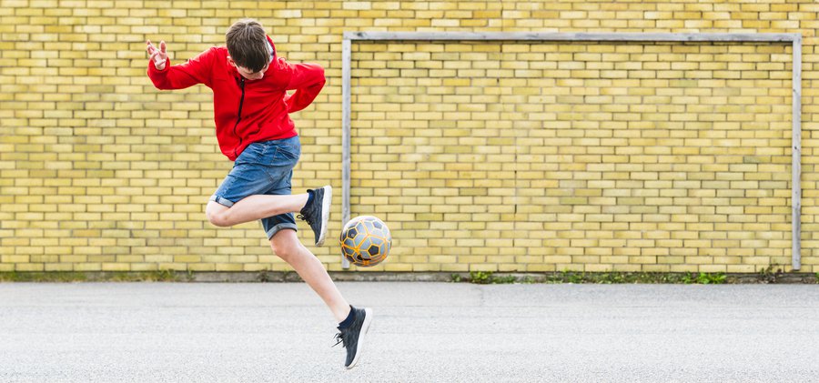 Pojke spelar fotboll på skolgård