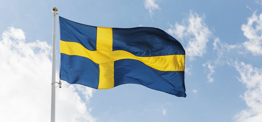 Sveriges flagga som böljar mot en blå himmel med vita moln.