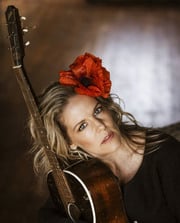 Porträttfoto av sångerskan Sofia Karlsson lutad mot sin gitarr med med röd blomma i håret .