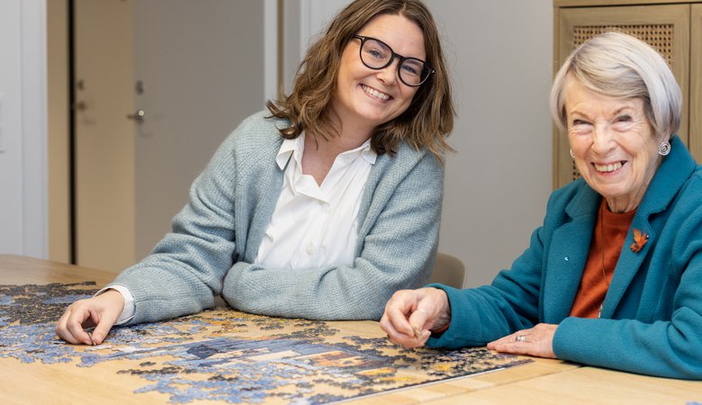 Äldre leende kvinna och glad personal som lägger pussel på en träffpunkt.