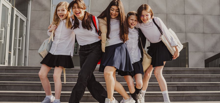 Happy schoolgirls enjoying together standing in front of school building